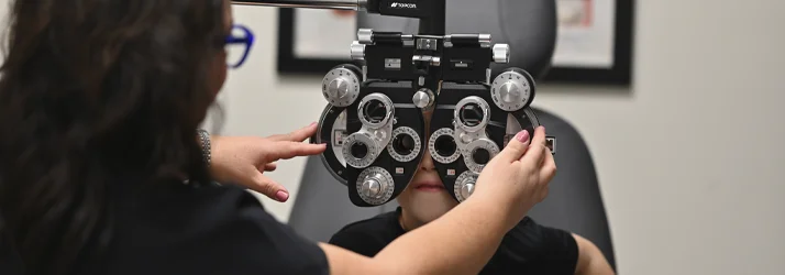 Eye‑care professional adjusting a phoropter during a detailed vision assessment for a boy.