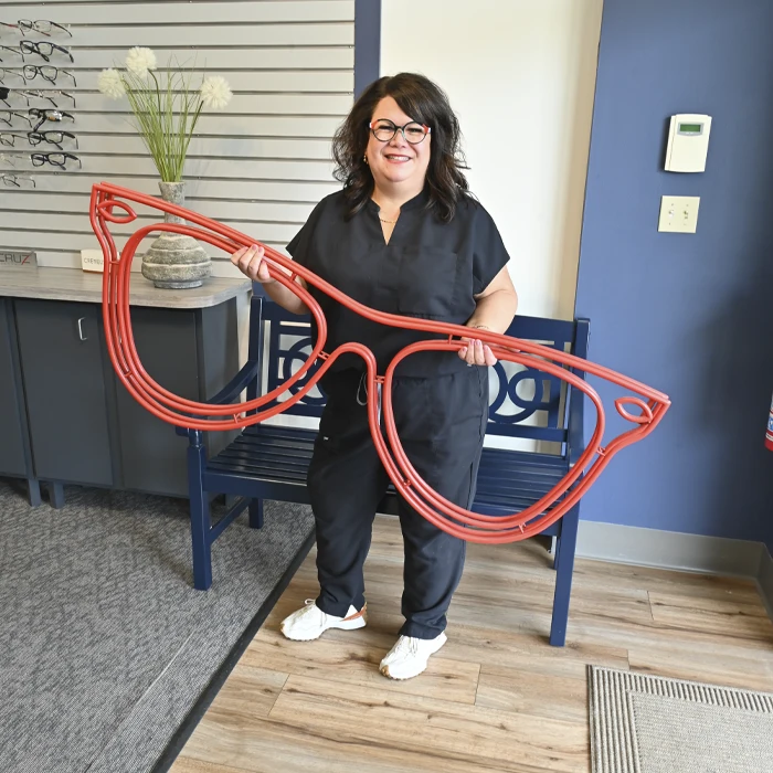 Dr. Jennifer Mentessi posing with oversized red glasses décor inside a stylish eyewear boutique.