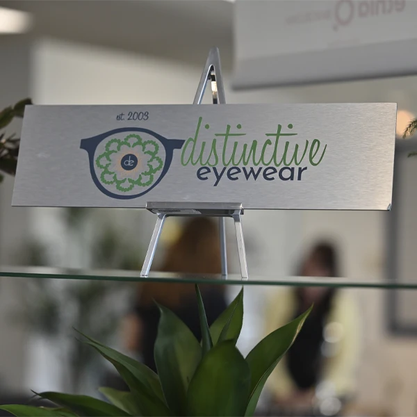 Central showroom display table showcasing a wide variety of eyeglass frames and plants.