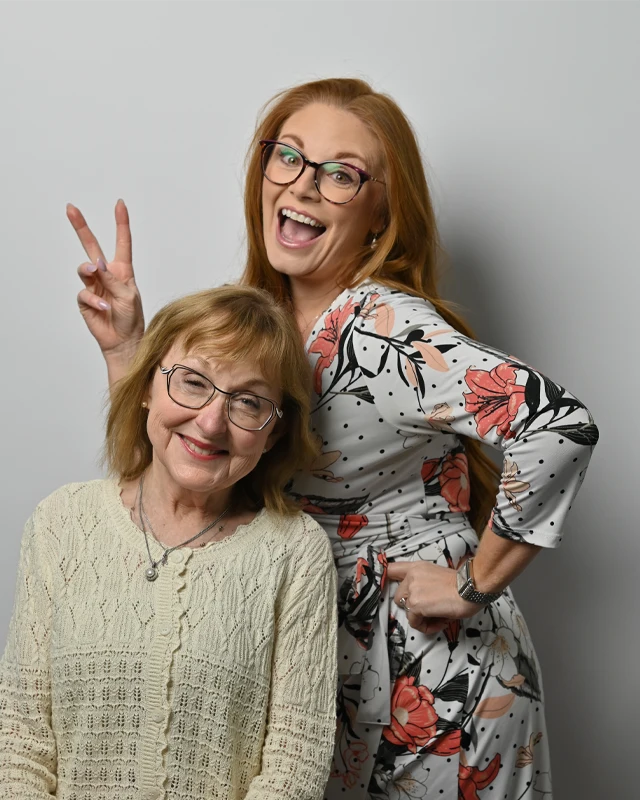 Two women smiling in a fun portrait, showcasing their eyewear with a lighthearted pose.