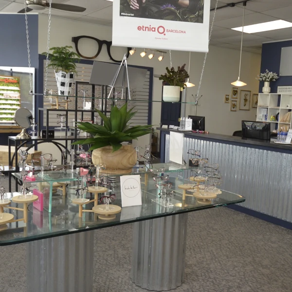Central showroom display table showcasing a wide variety of eyeglass frames and plants.